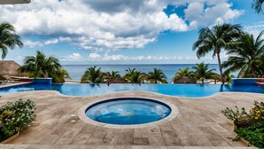 A pool area with a view of the ocean, palm trees, and a thatched-roof structure. - Ocean paradise - Relax & refresh - Villa Paradiso (San Miguel de Cozumel)