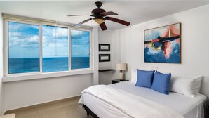 A bedroom with a large window, a ceiling fan, a bed with white and blue bedding, and a painting on the wall. - Ocean paradise - Relax & refresh - Villa Paradiso (San Miguel de Cozumel)