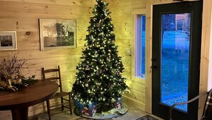 Una habitación acogedora con detalles de madera, un árbol de Navidad, una mesa de comedor y una alfombra estampada.