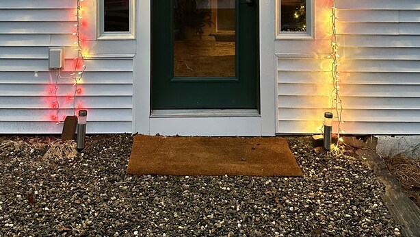 Una casa con puerta verde, dos coronas adornadas con lazos rojos y luces de cadena.