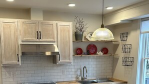 Una cocina moderna con armarios blancos, una isla de madera con taburetes, horno empotrado e iluminación colgante.