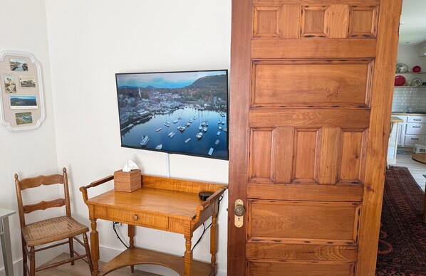 Une porte en bois au design traditionnel, un téléviseur fixé au mur diffusant un paysage pittoresque, et une chaise en bois avec un coussin.