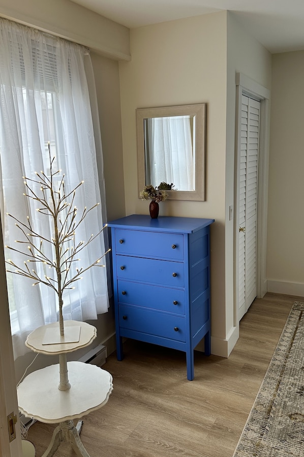 Ein Zimmer mit einer blauen Kommode, einem weißen Tisch mit einer dekorativen Zweig und einem Spiegel über der Kommode sowie einer Tür mit Fensterläden.