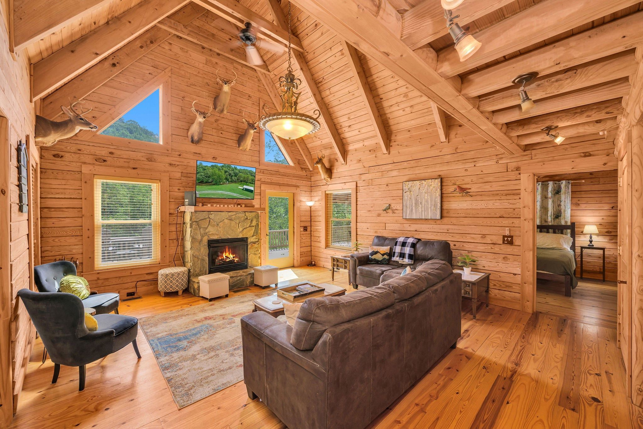 A log cabin interior with a fireplace, leather sofa, and a television.
