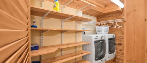 A laundry room with wooden shelves, a washing machine, and a detergent bottle.