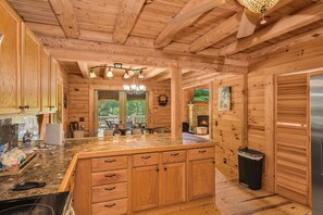 A wooden cabin interior with a kitchen featuring a large island, wooden cabinets, and a stone fireplace.