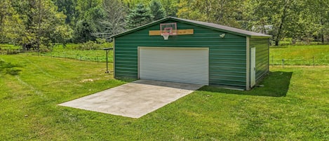 A green metal shed with a basketball hoop, a garage door, and a concrete ramp leading to the entrance.