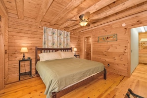 A wooden-paneled bedroom with a bed, two bedside tables, a ceiling fan, and a door.