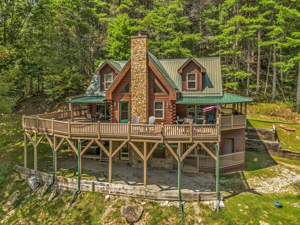 A cabin with a stone chimney, a deck, and a covered porch.