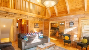 Interior acogedor de una cabaña con techo de madera, un sofá con cojines decorativos, una mesa de centro y un comedor con sillas y una mesa.