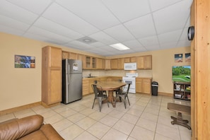 A compact kitchen with wooden cabinets, a refrigerator, a microwave, and a dining table with chairs.
