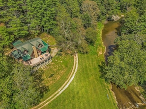 Una casa con techo verde, rodeada de césped y un río.
