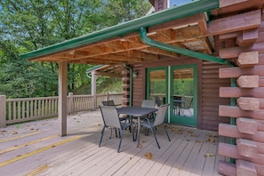 A wooden deck with a covered patio area, outdoor seating, and a view of the surrounding forest.
