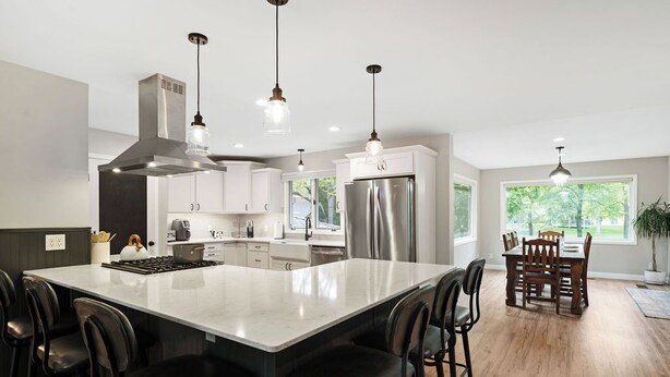 A modern kitchen with a large island, stainless steel appliances, pendant lighting, and a dining area with wooden chairs. - Pets & Kids Love this Montana Dream Home! (Billings)