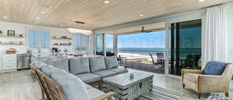 A modern kitchen with a large island, a dining area with a view of the beach, and a living room with a sofa and coffee table.