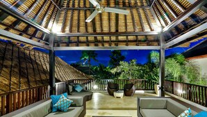 An outdoor seating area with cushioned sofas and a central coffee table, surrounded by a wooden fence and potted plants. - The Residence Seminyak (Seminyak)