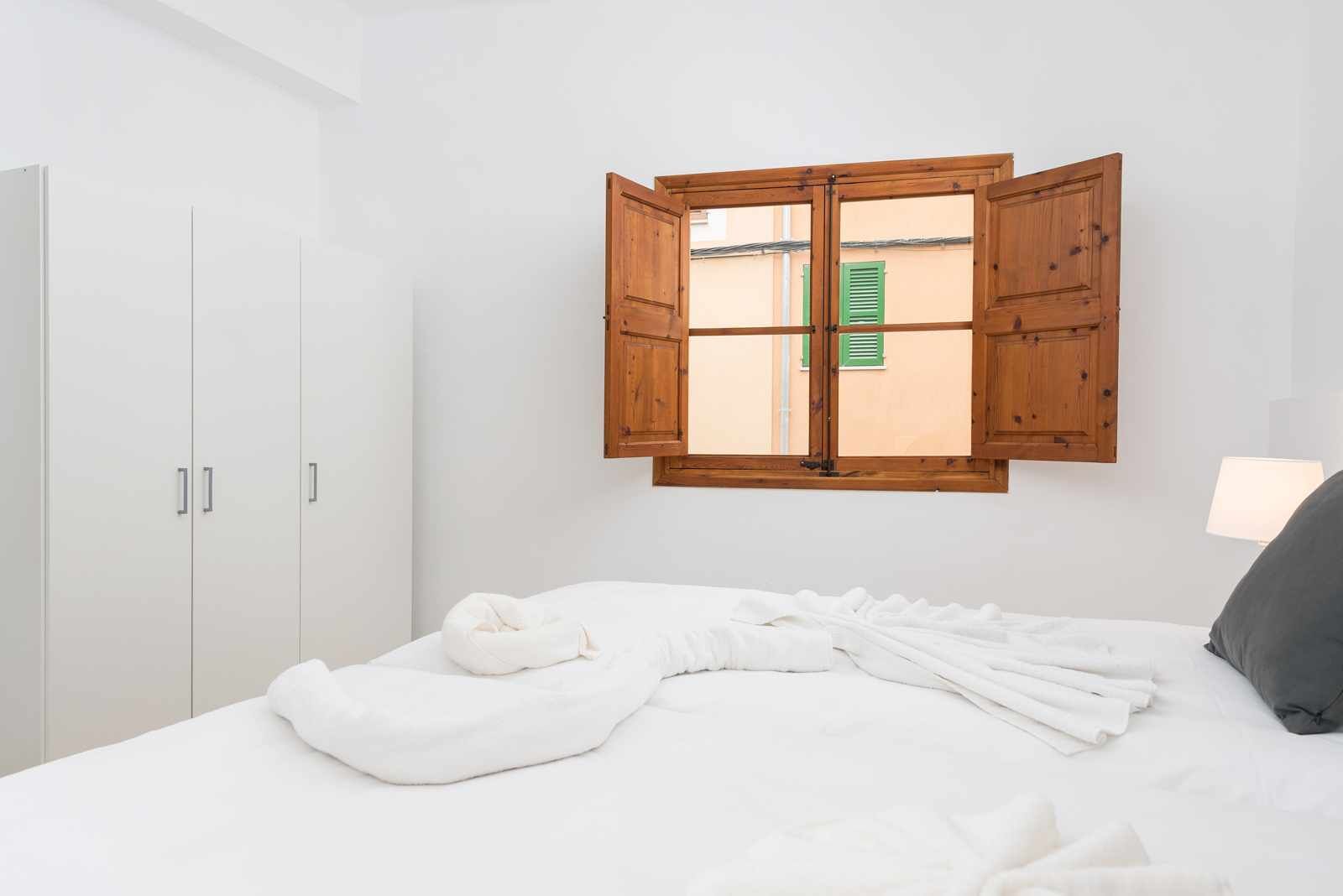 Un dormitorio con cama, armario de madera y ventana con contraventanas.