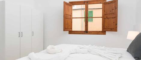 Un dormitorio con cama, armario de madera y ventana con contraventanas.