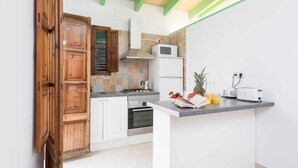 Cocina con armarios blancos, una puerta de madera, estufa, microondas y una pequeña isla con frutas y un libro.