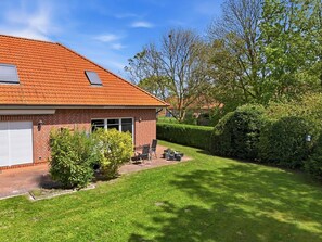 A brick house with a red-tiled roof, a garage, and a well-maintained lawn with a patio area.