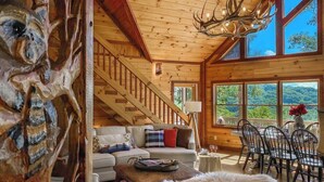 A wooden interior with a staircase, a dining area, and large windows offering a view of the outdoors. - Experience North GA Mtn Retreat: Views w/ Hot Tub (Morganton)