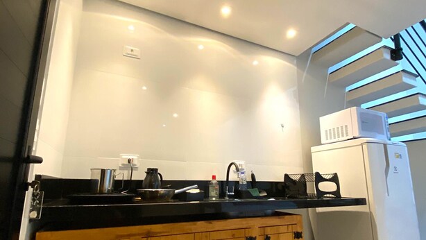 A modern kitchen with a wooden cabinet, a white refrigerator, and a black countertop. - Duplex apartment in Villa Licuri (são sebastião)