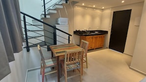 A compact living space with a dining area, kitchenette, and a staircase. - Duplex apartment in Villa Licuri (são sebastião)