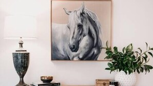 Una sala de estar con un aparador de madera, un cuadro de un caballo enmarco, una lámpara, una planta y un sofá azul.