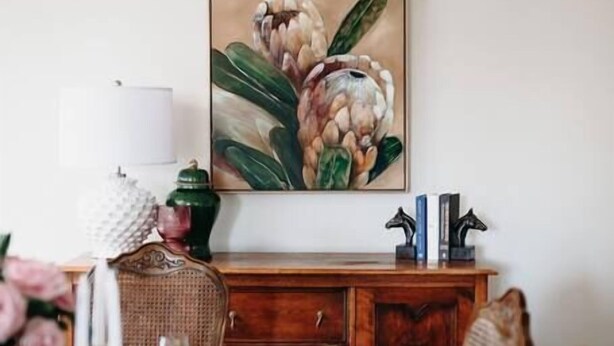 Un comedor con una mesa de madera dispuesta para dos, un cuadro sobre la mesa y un aparador debajo.