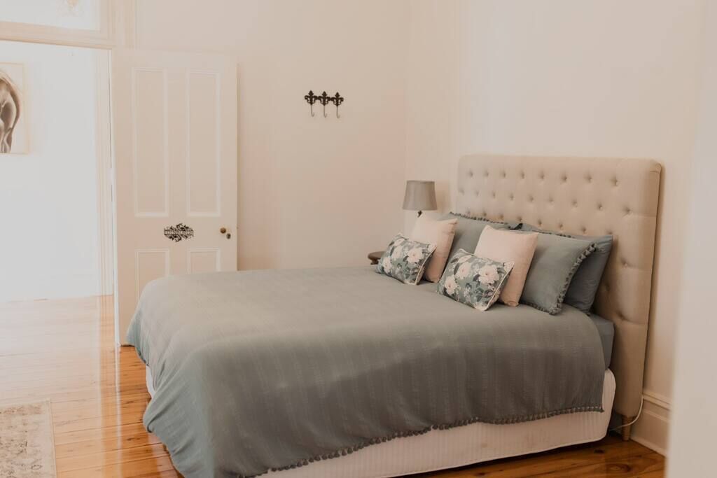 A bedroom with a tufted headboard, a grey bedspread, and floral-patterned pillows.
