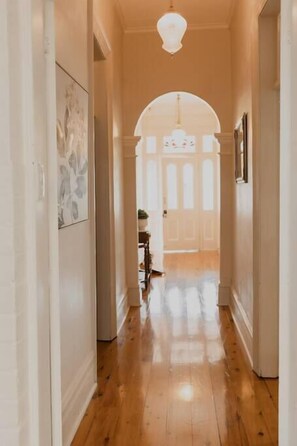 Un pasillo con suelo de madera, paredes blancas y un amplio arco que da a otra habitación.