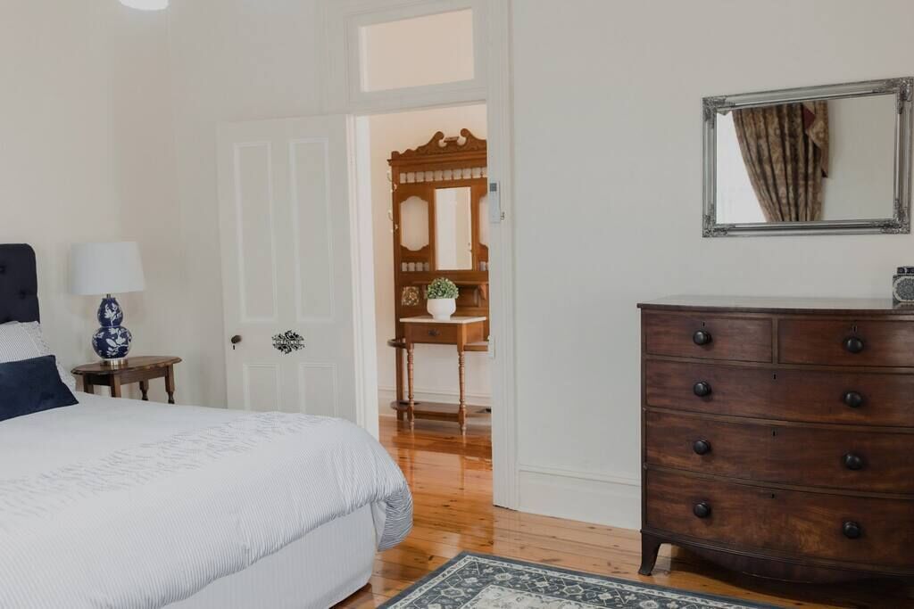 Une chambre à coucher comprenant un lit, une commode, un miroir et une porte donnant sur une autre pièce.