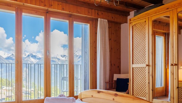 Habitación de cabaña de madera con cama, toallas y vistas a montañas a través de amplios ventanales.