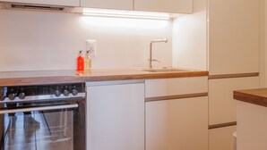 Una cocina moderna con armarios blancos, un horno de acero inoxidable, un lavamanos y una encimera con detalle de madera.