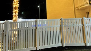 Een witte hek, een palmboom en lichtjes aan een gebouw in de nacht.