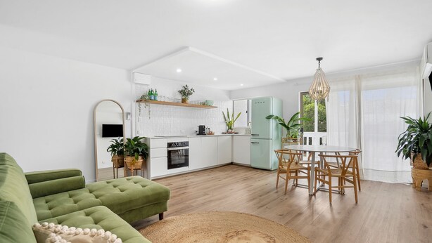 Een moderne keuken met witte kasten, een groene koelkast, en een eethoek met een houten tafel en stoelen.