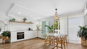 Een moderne keuken met witte kasten, een inbouwoven en een eethoek met een ronde tafel en stoelen.