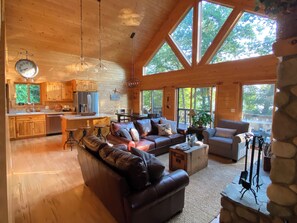 Una cabaña espaciosa con una amplia sala de estar, una cocina y múltiples ventanas que ofrecen vistas del bosque circundante.