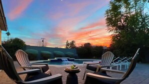 Ein Sitzbereich im Freien mit Adirondack-Stühlen und einem runden Tisch, mit Blick auf einen Pool mit Wasserfall.