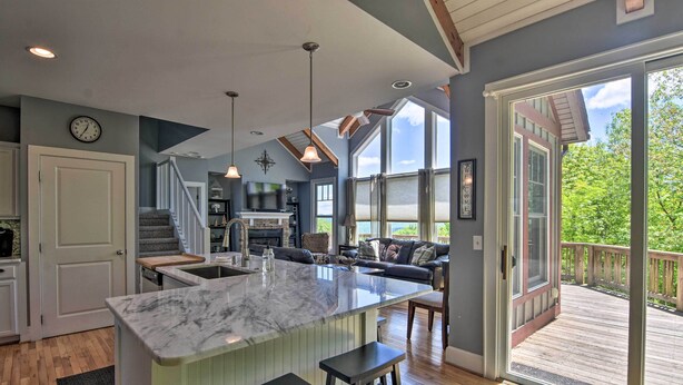 A spacious kitchen with a marble island, wooden flooring, and a large window overlooking a deck.