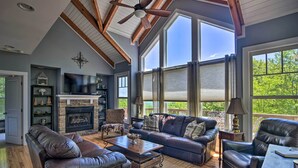 A spacious living room with leather sofas, a fireplace, and large windows offering a view of the outdoors.