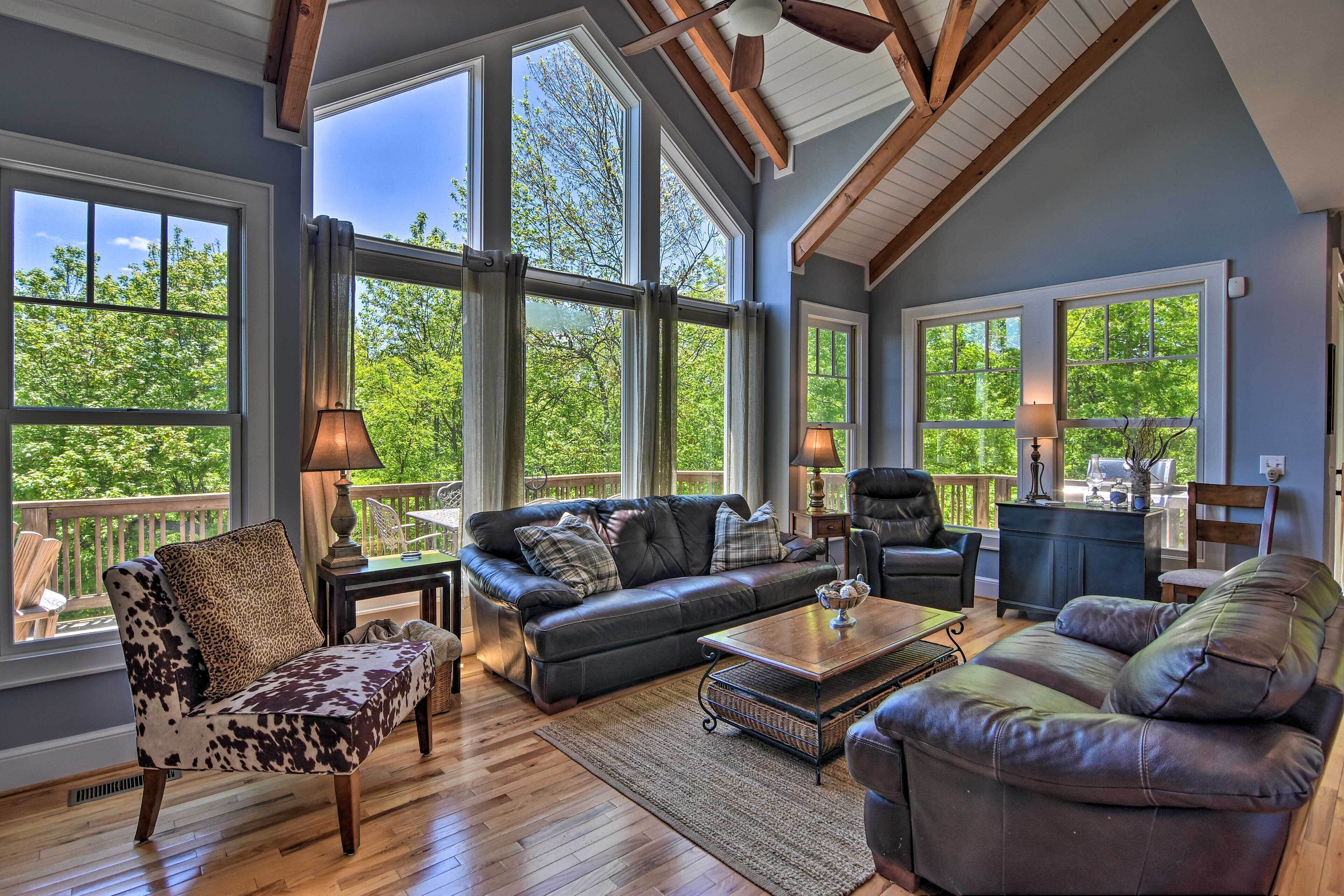 A spacious living room with large windows, a leather sofa, a coffee table, and a fireplace.