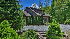 A house with a sloped roof, a large window, and a gravel driveway surrounded by trees.