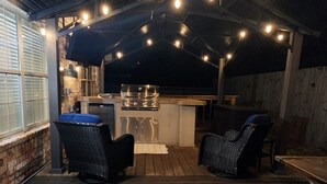 An outdoor patio area with a wooden deck, two wicker chairs, a small table, and a grill station.