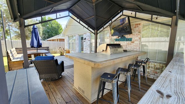 An outdoor bar area with a stone countertop, bar stools, and a grill.