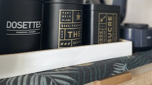 Ein Regal mit drei schwarzen Behältern, beschriftet mit 'DOSETTES', 'THÉ' und 'SUCRE'.