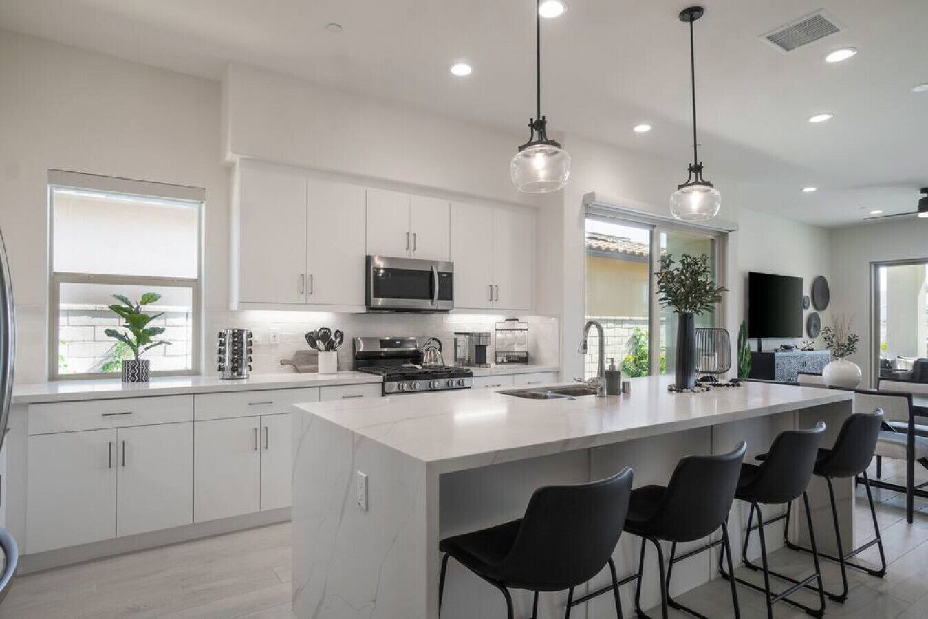 Una cocina moderna con armarios blancos, una isla grande con taburetes de bar, electrodomésticos de acero inoxidable e iluminación colgante.