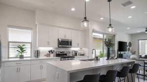 A modern kitchen with white cabinets, a large island with bar stools, stainless steel appliances, and pendant lighting. - Private pool & hot tub w/ mountain views (La Quinta)