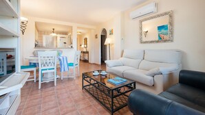 Una sala de estar con un sofá blanco, un sofá de cuero negro, una mesa de centro y un comedor con sillas y una mesa.