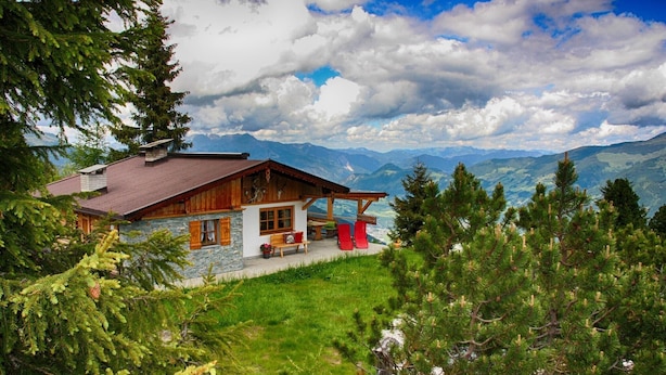 Un chalet doté d’une façade en pierre, d’un toit en bois et d’un balcon offrant une vue sur un paysage montagneux.